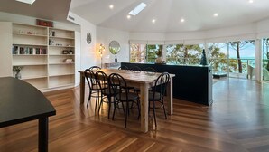 A modern kitchen with a wooden dining table and chairs, a built-in bookshelf, and a large window offering a view of the sea. - Spacious 4-Bed Home with Coastal Charm (Long Beach)