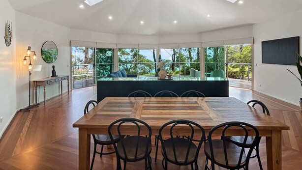 A spacious dining area with a large wooden table and black chairs, a glass partition with a view of greenery, and a modern ceiling design with recessed lighting. - Spacious 4-Bed Home with Coastal Charm (Long Beach)