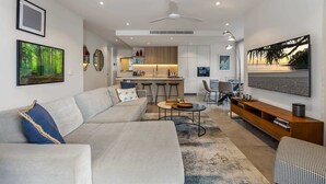 Een moderne woonkamer met een bank, salontafel en televisie. Er is een keukenhoek met een bar en krukken.