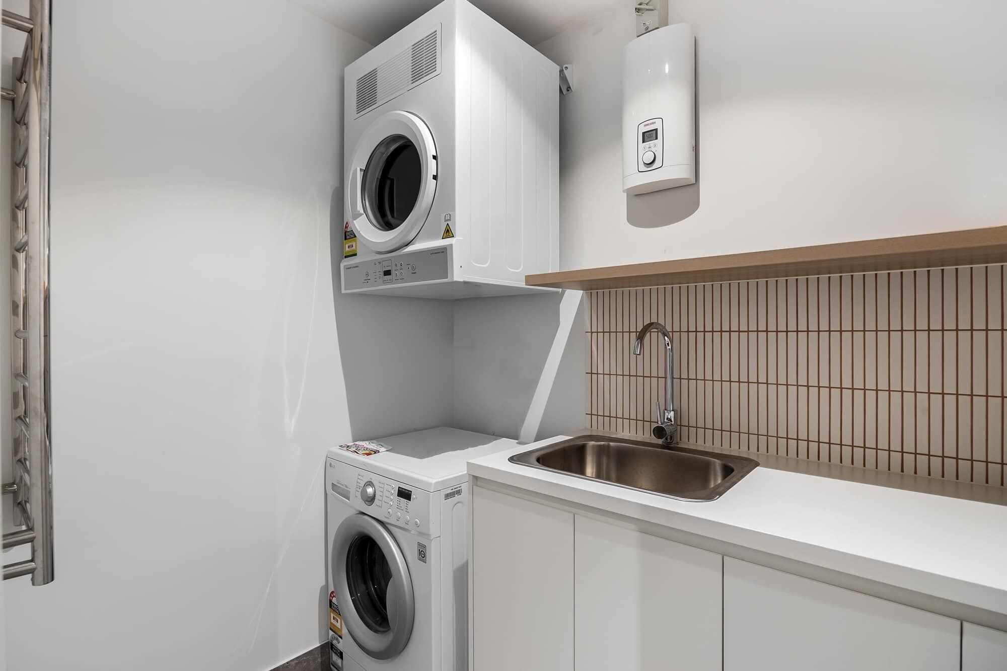 A compact kitchen with a built-in washer and dryer, a stainless steel sink, and a wall-mounted heater.