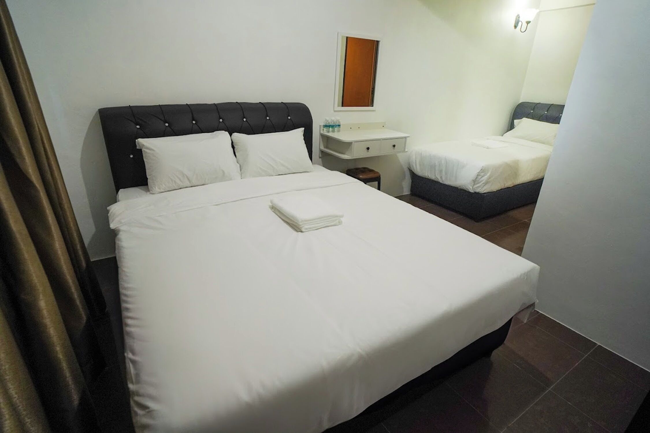 Una habitación de hotel con una cama grande, una cama más pequeña, una mesita de noche y un espejo.