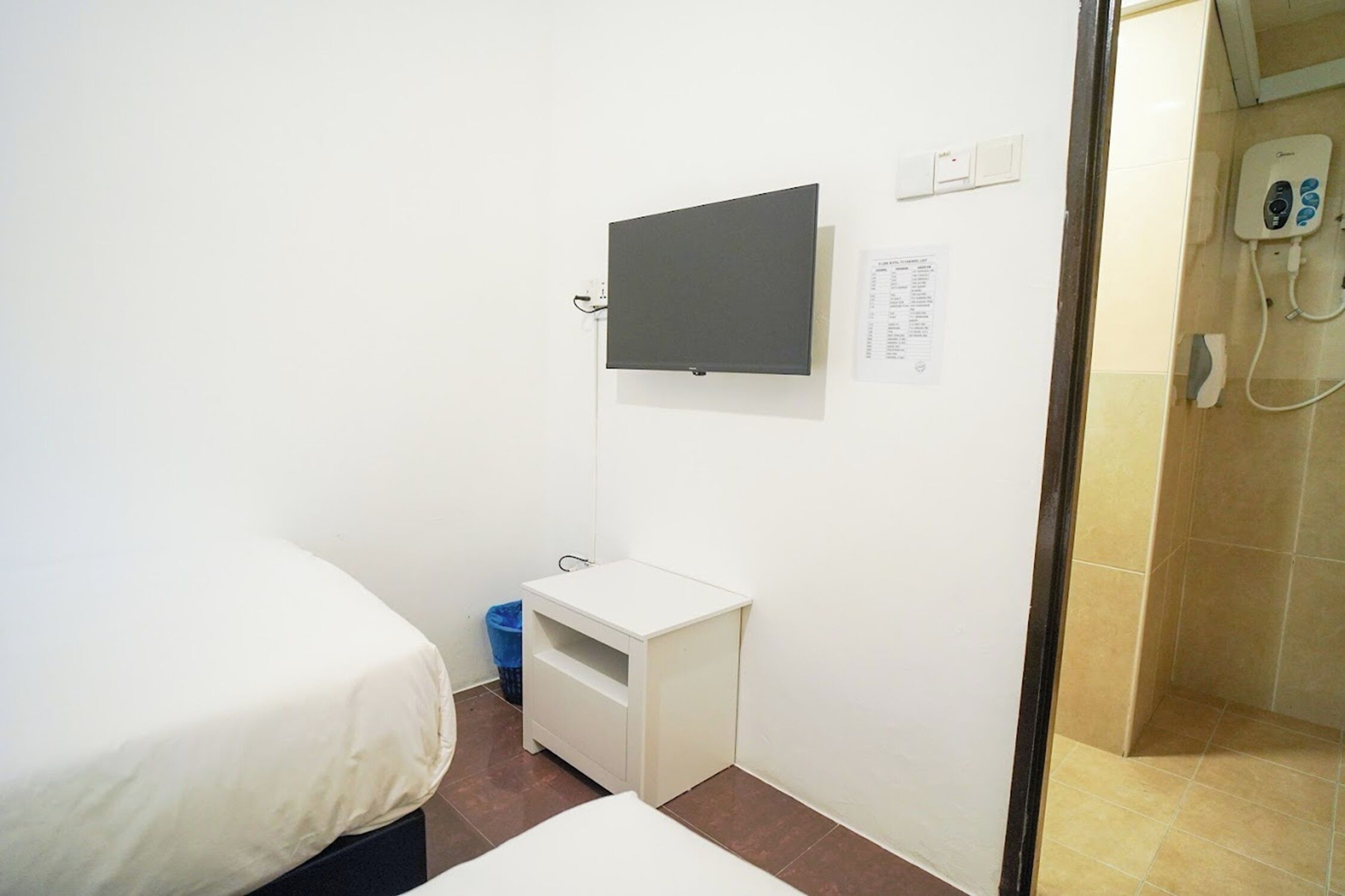 A small, clean room with a bed, a small white table, a mounted TV, and a telephone.