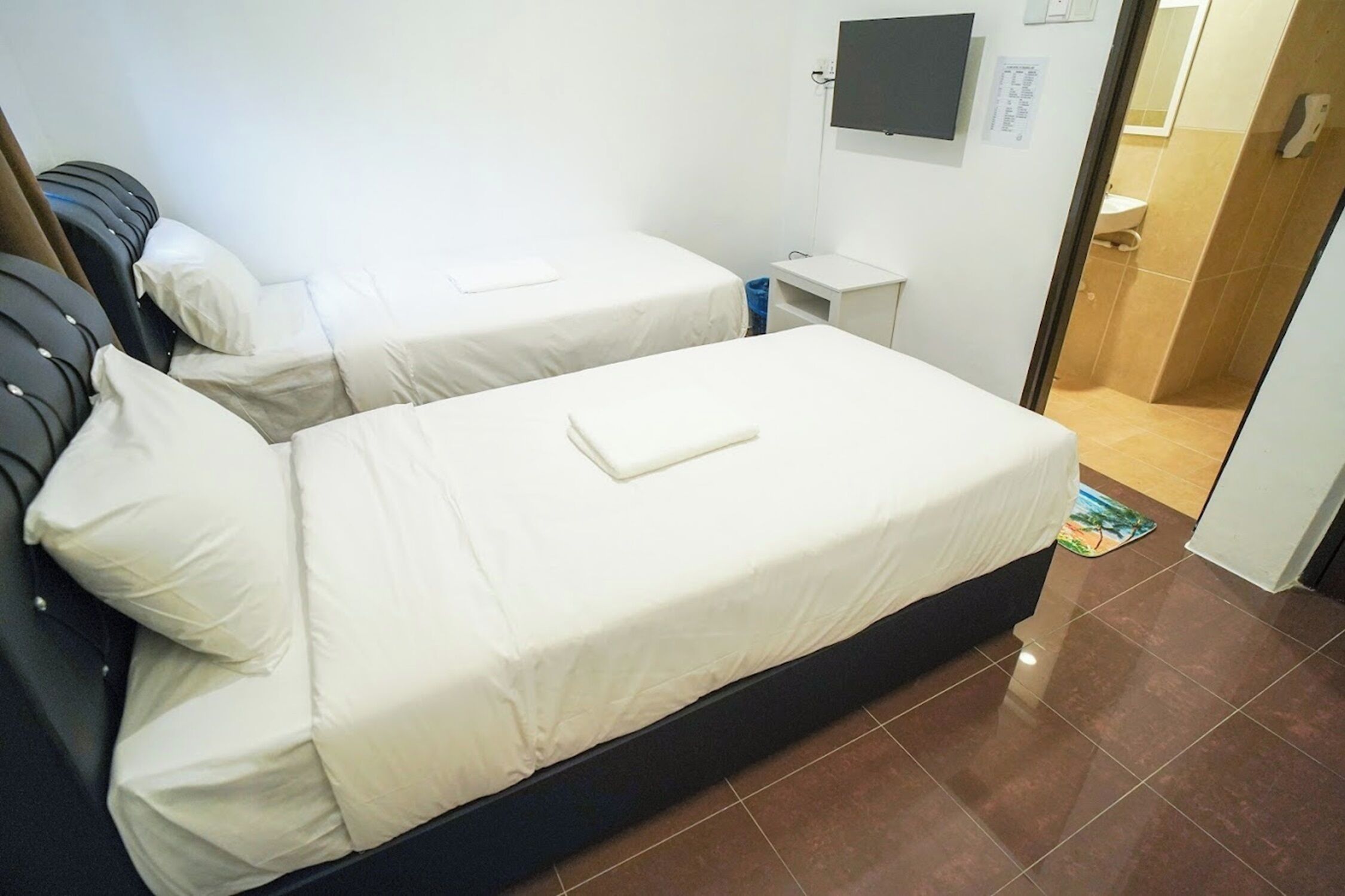 Une chambre d’hôtel avec deux lits, une télévision, une petite table et une salle de bain visible à travers une porte ouverte.