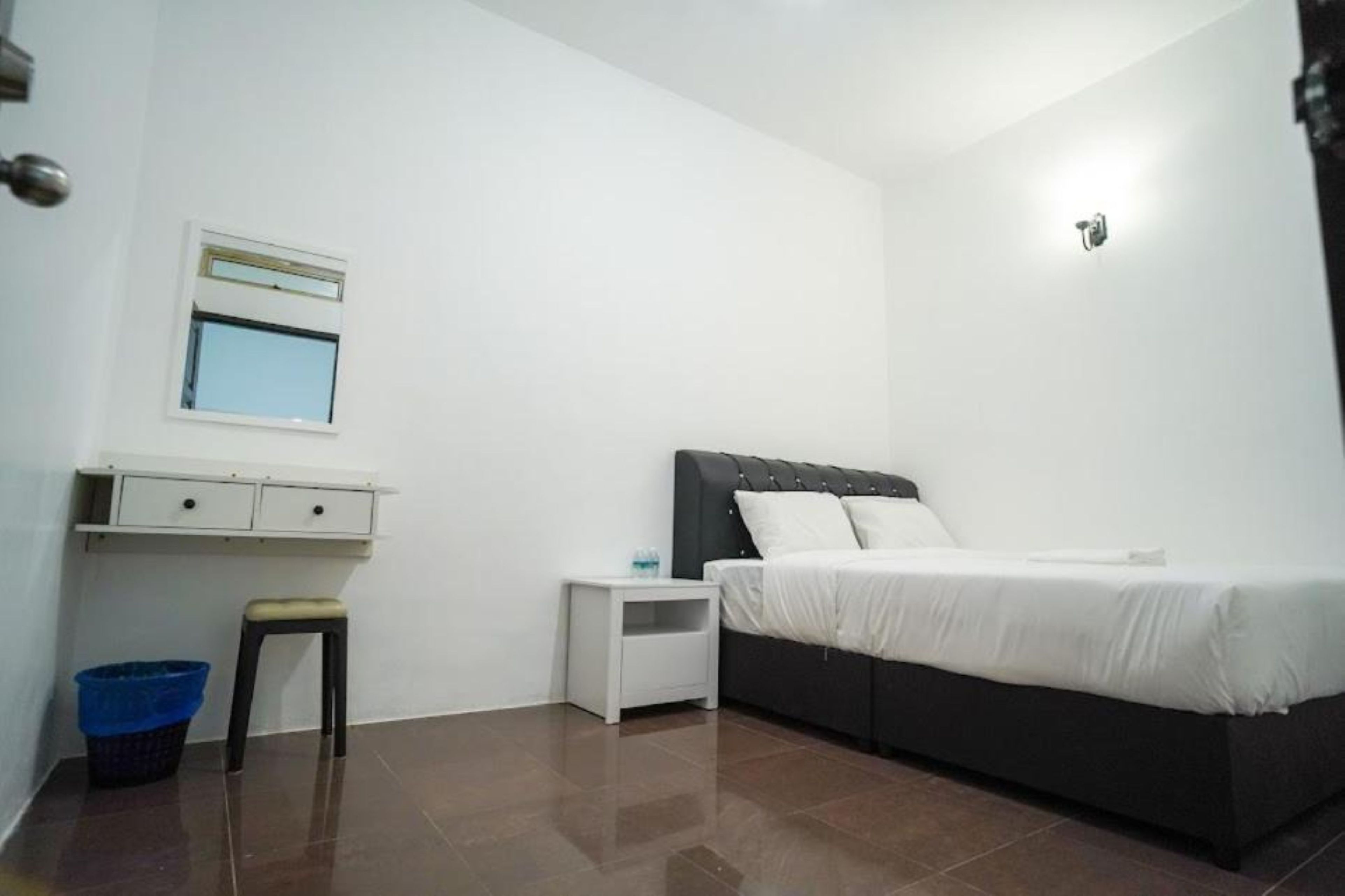 Une chambre à coucher comprenant un lit, une table de chevet, un petit tabouret, une fenêtre et un luminaire fixé au mur.