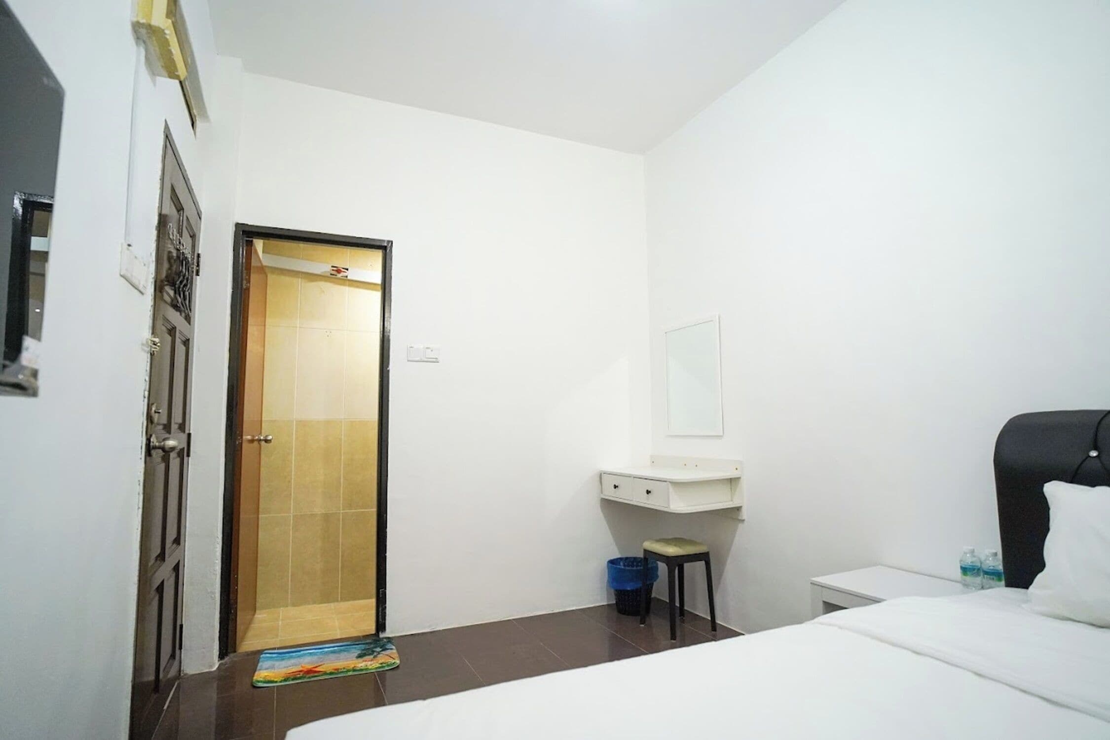A hotel room with a bed, a small desk with a chair, a bathroom with a shower, and a door.