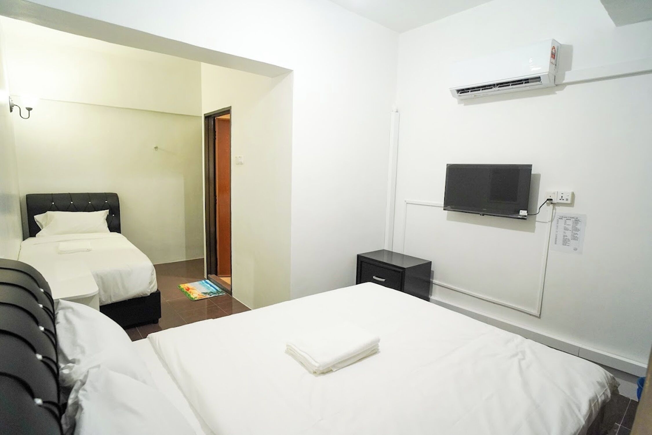 A hotel room with two beds, a TV, an air conditioner, and a small bedside table.