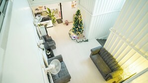 A spacious living area with a grey sofa, a white fan, and a Christmas tree. - B Link Hotel (Kulai)