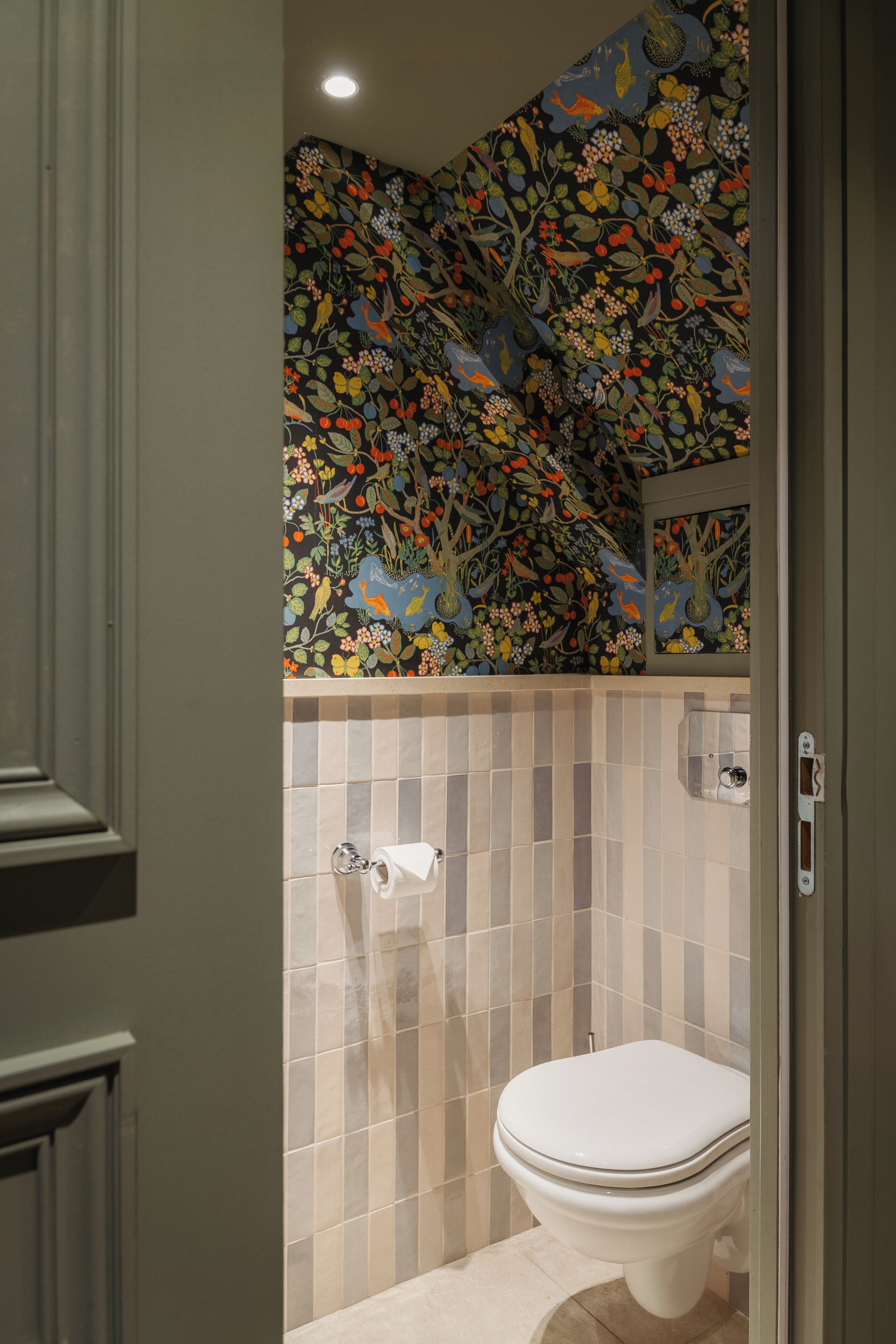 Une salle de bain avec des toilettes, des murs carrelés et un papier peint à motifs floraux.