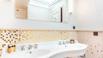A bathroom with a white sink, gold mosaic tiles, a large mirror, and a skylight.
