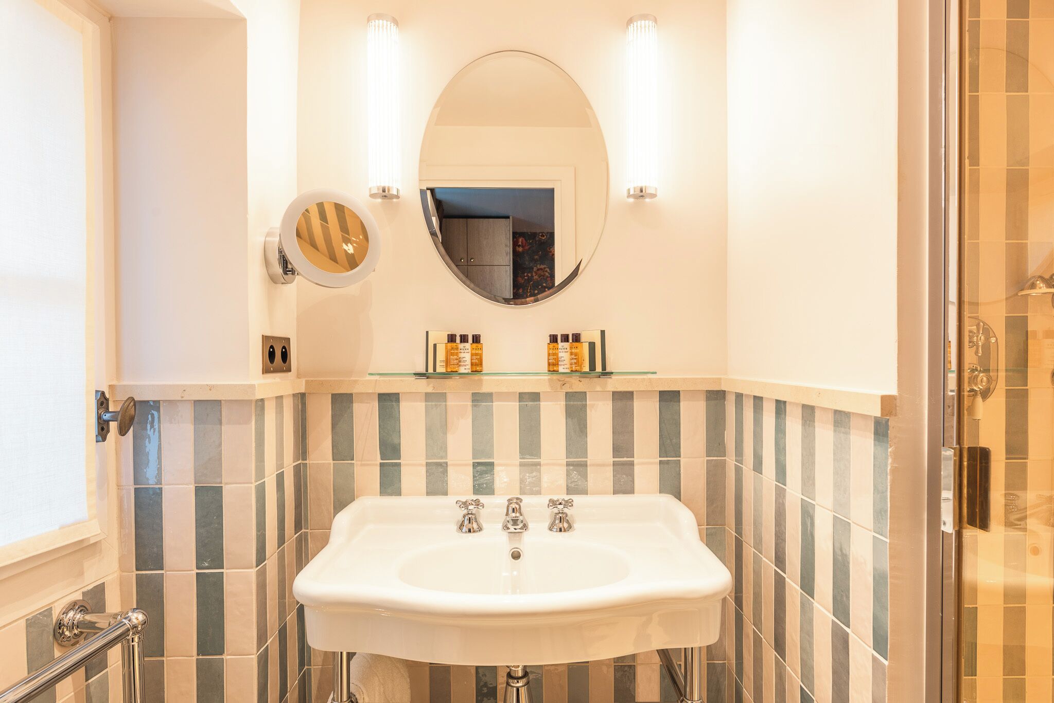 A bathroom with a white sink, two wall-mounted lights, a mirror, and striped tiles.