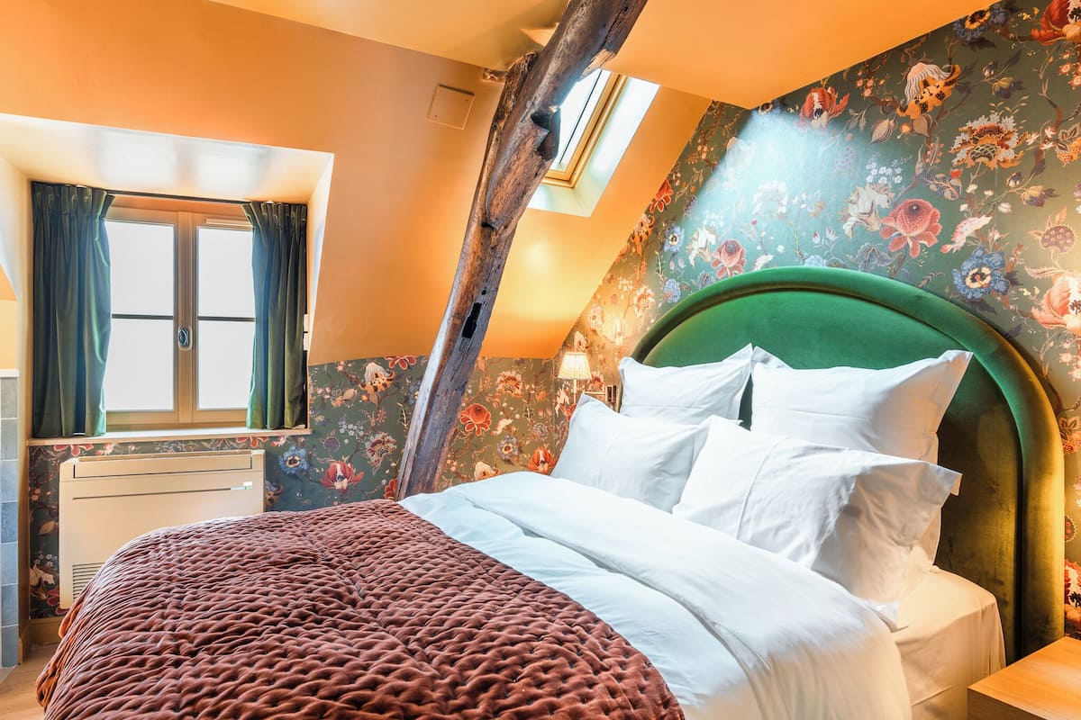A bedroom with a large bed, floral wallpaper, a skylight, and a wooden headboard.