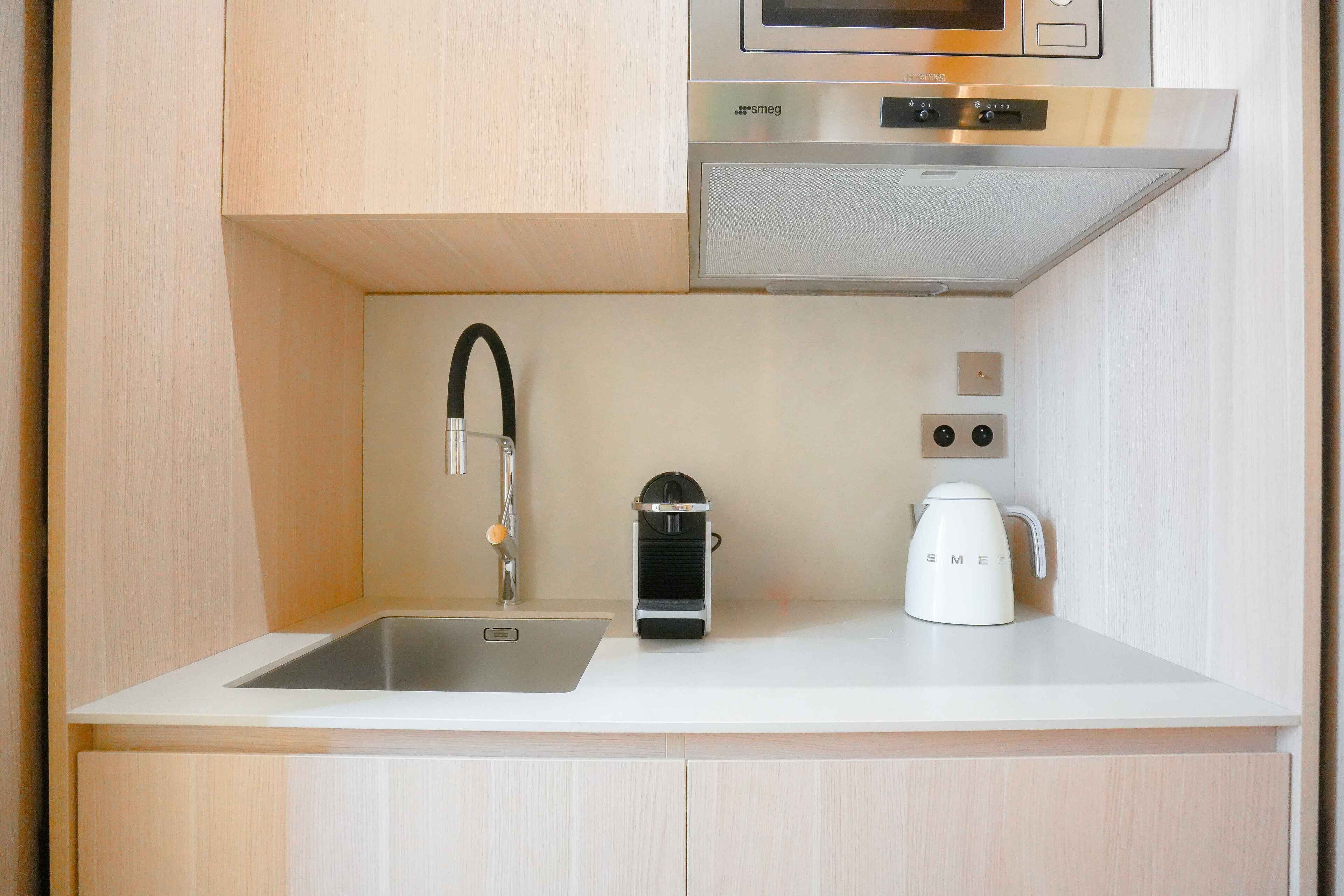 Une cuisine compacte dotée d’un évier en acier inoxydable, d’une machine à café et d’un four à micro-ondes placé au-dessus du plan de travail.