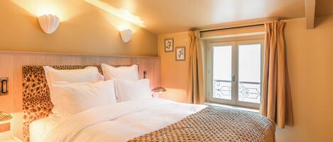 A neatly made bed with a patterned bedspread, a headboard with a leopard print design, and a wall-mounted light fixture.