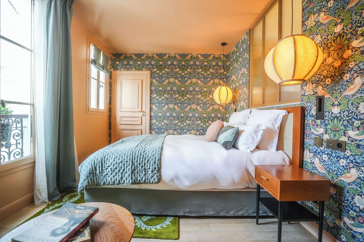 A bedroom with a bed, a bedside table, a lamp, and a window with curtains.