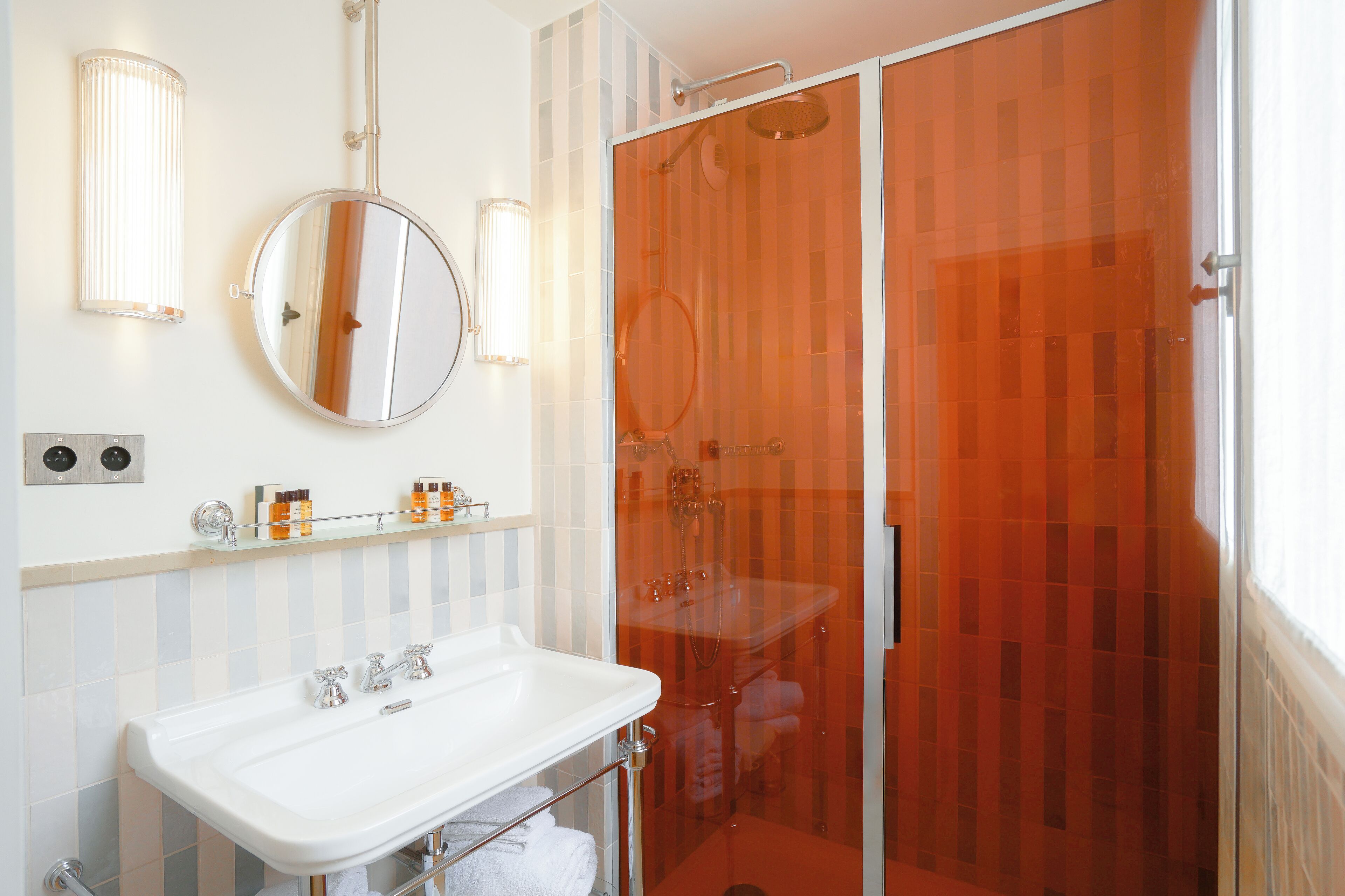 A bathroom with a white sink, a round mirror, and a glass-enclosed shower.