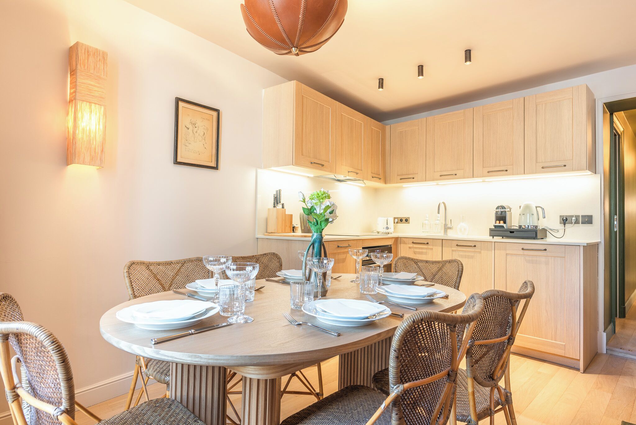 A dining area with a round table set for six, surrounded by wicker chairs.