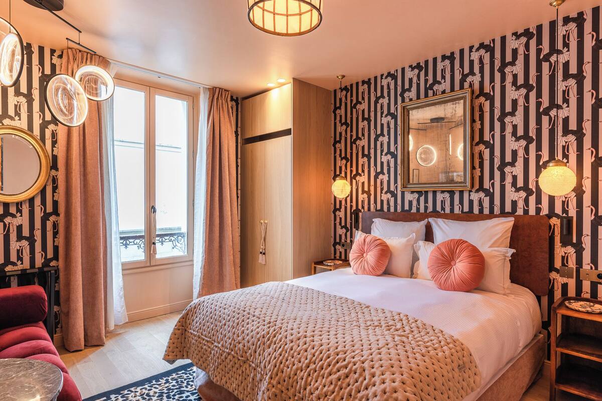 A bedroom with a large bed, a nightstand, a mirror, and a view of the outside.