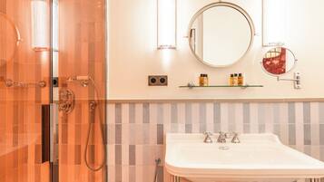 Un bagno con box doccia in vetro, lavandino bianco con due rubinetti e specchio rotondo sopra il lavandino.