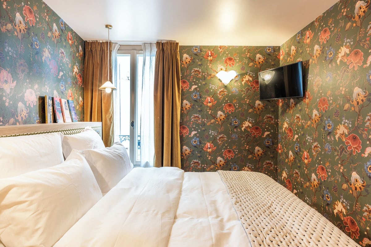 A hotel room with a bed, a TV mounted on the wall, and a window with curtains.