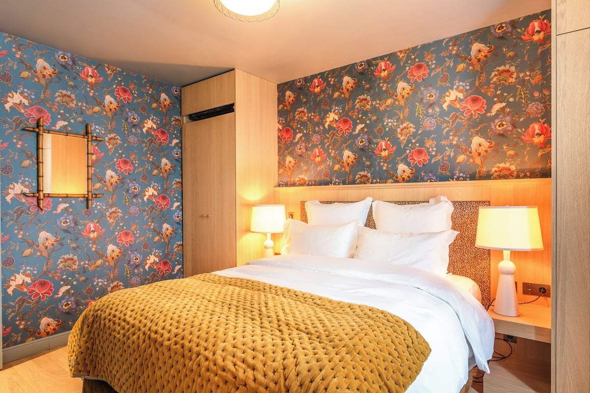 A bedroom with a floral wallpaper, a bed with white linens, and two bedside lamps.