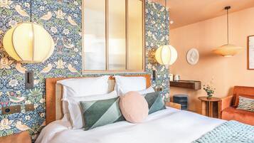 A bedroom with a bed, a wooden headboard, a large mirror, and a wall with floral wallpaper.