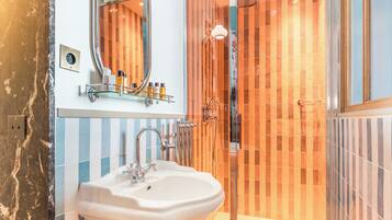 Un baño con lavamanos blanco, un espejo y una ducha con azulejos anaranjados.
