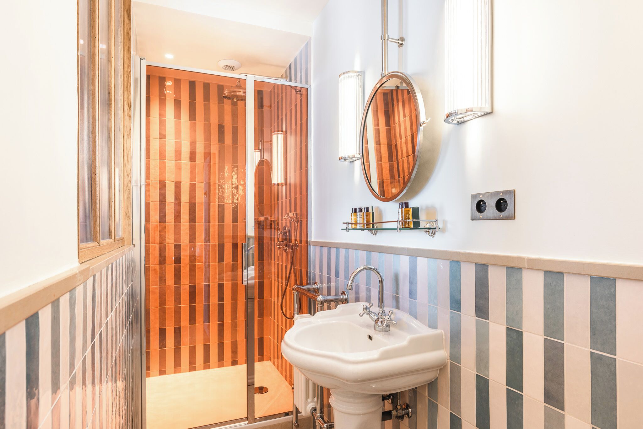 A bathroom with a glass-enclosed shower, a white sink, and striped tiles.