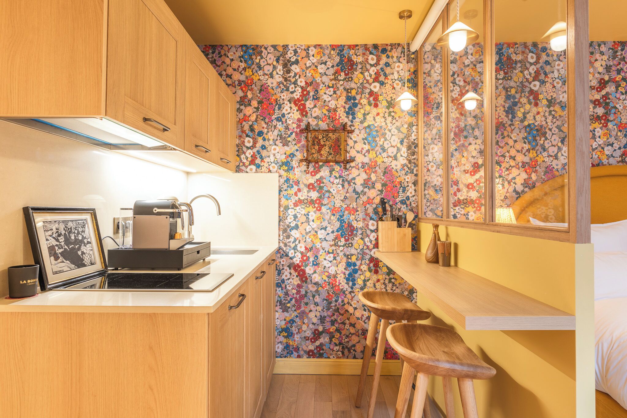 A compact kitchen with wooden cabinets, a countertop with a coffee machine, and a floral-patterned backsplash.