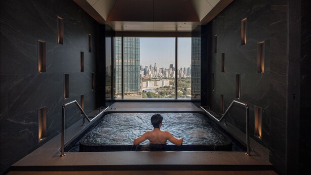 A man in a modern indoor pool with a cityscape view through large windows.