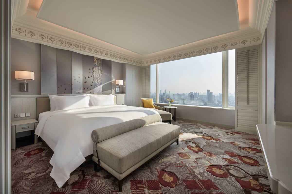 Une chambre d’hôtel avec un grand lit, un canapé, une petite table et une vue sur le panorama de la ville.