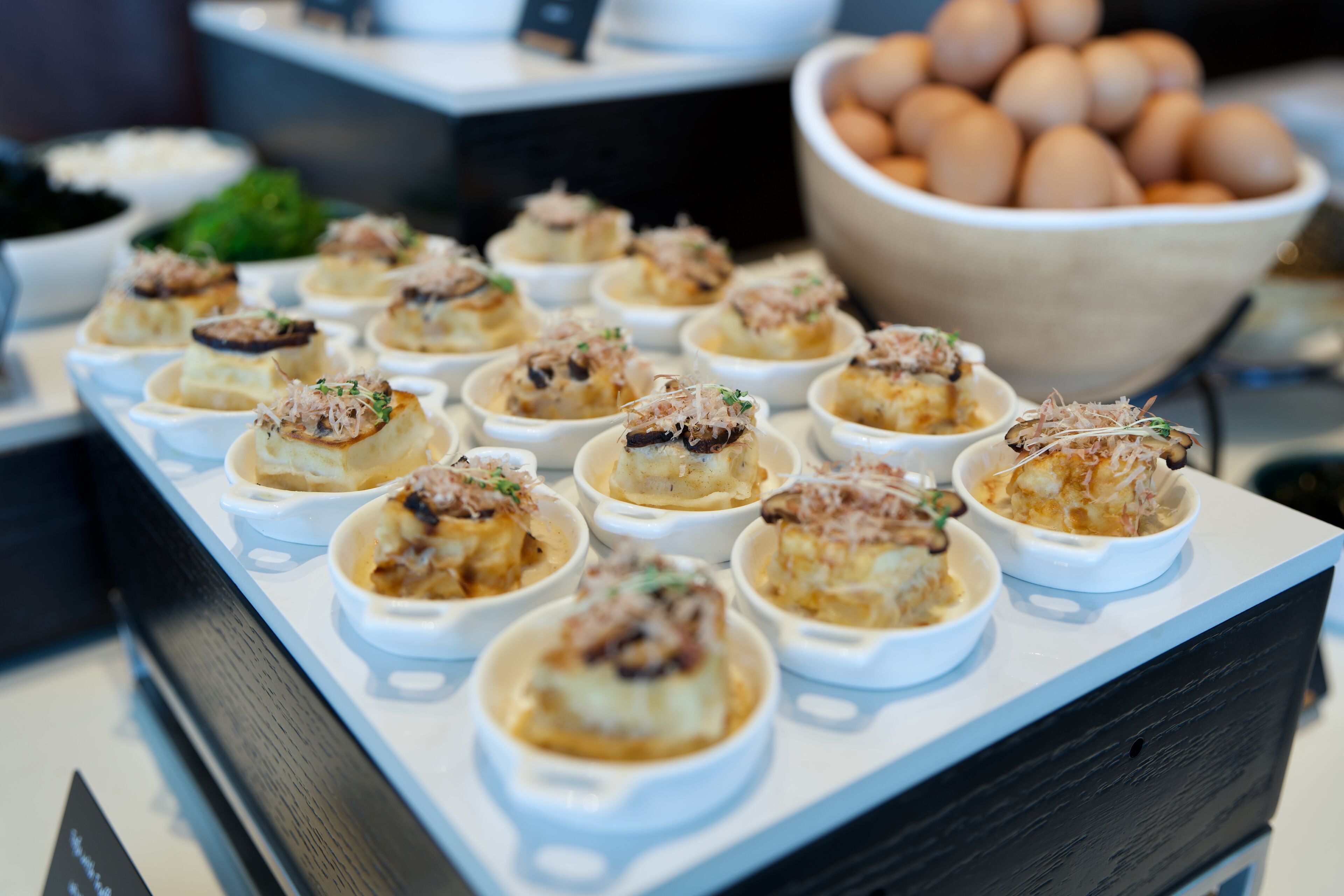 A buffet table with small bowls of food, a bowl of eggs, and a blackboard in the background.