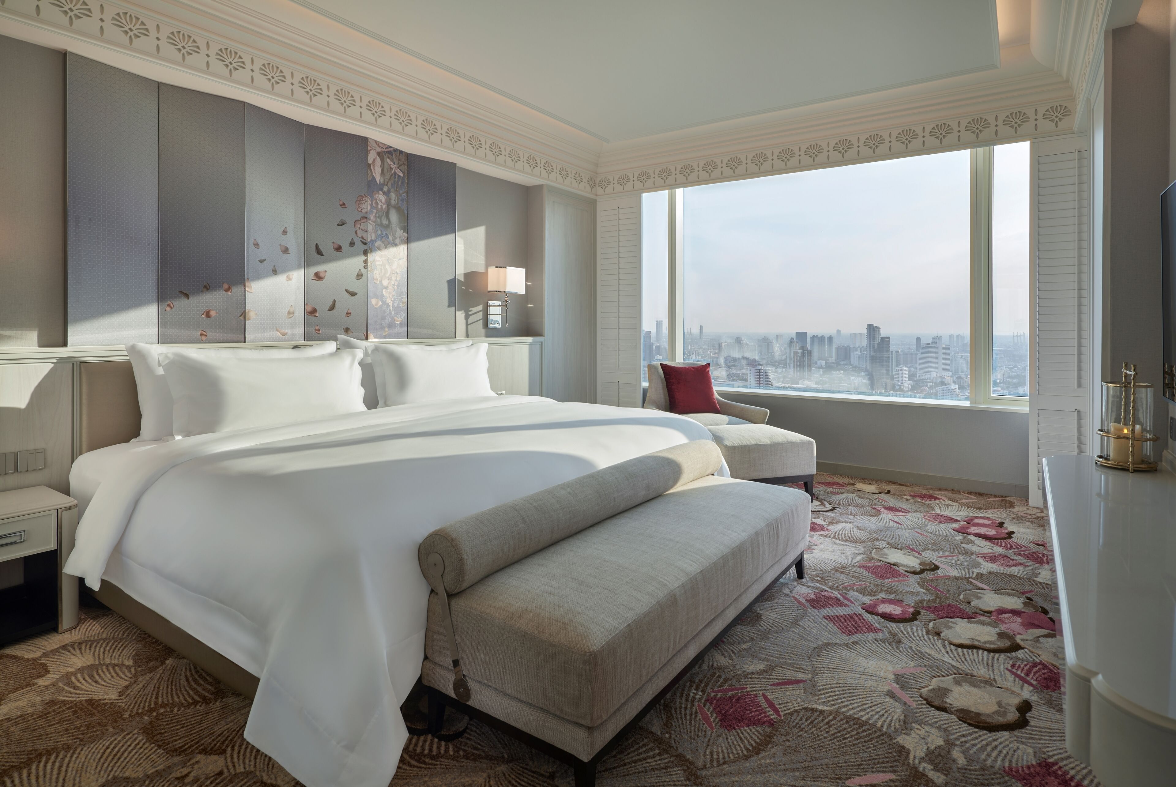 Ein geräumiges Hotelzimmer mit einem großen Bett, einer Sitzecke, Blick auf die Stadt und einem dekorativen Kopfteil.