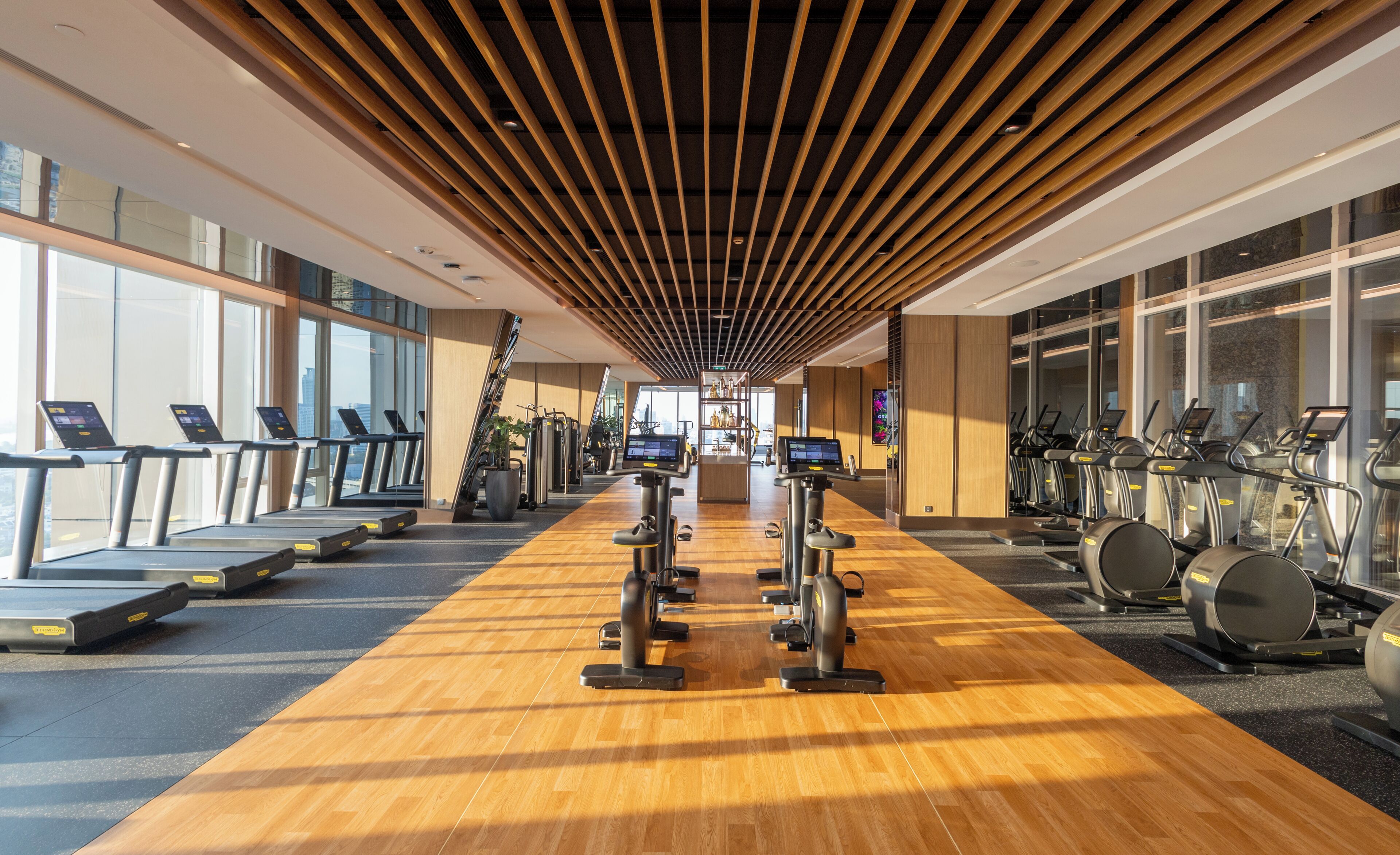 A modern gym with treadmills, elliptical machines, and a wooden floor.