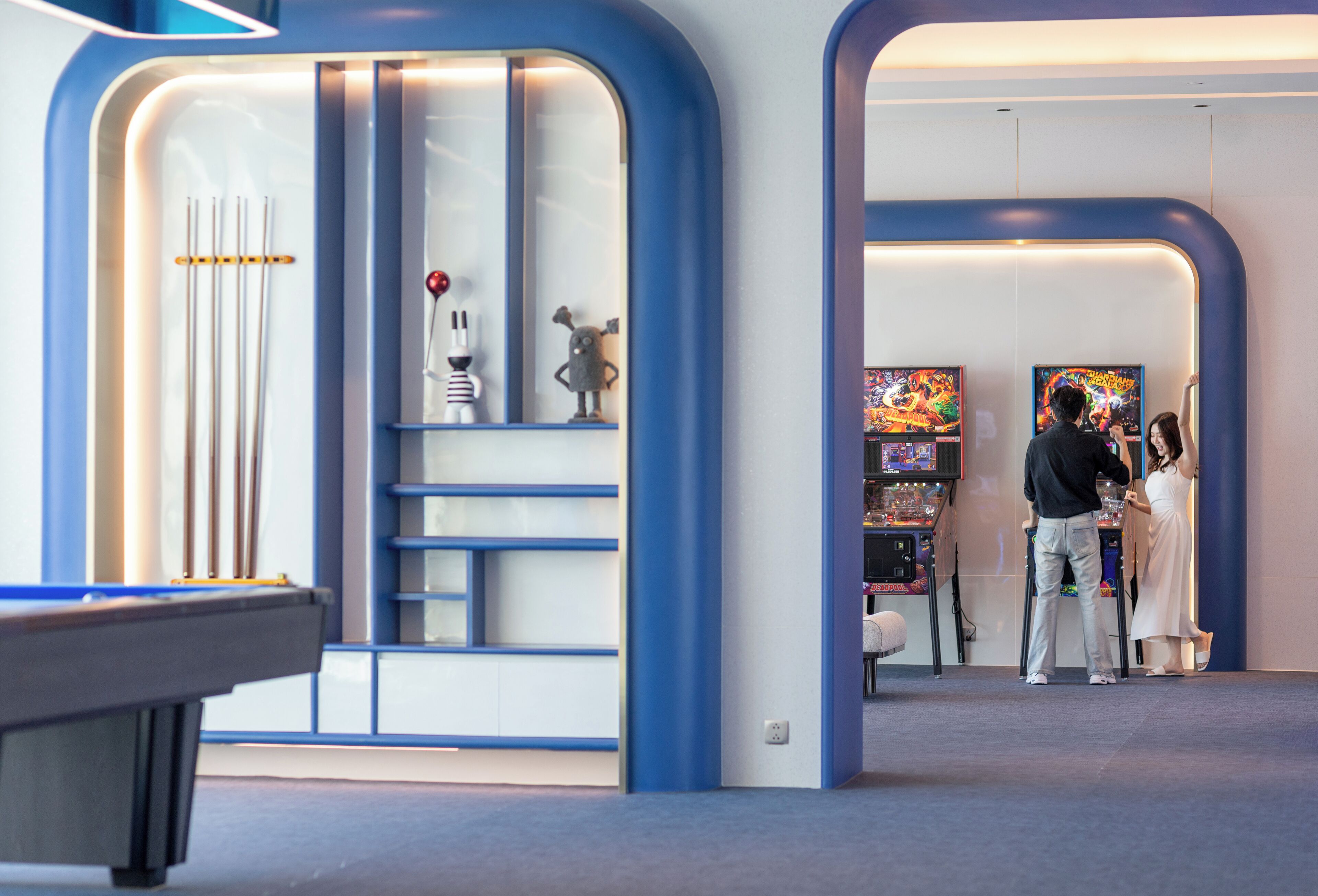 A modern interior with a pool table, a game area with arcade machines, and a seating area with a white sofa.