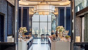 A modern hotel lobby with a central reception desk, seating area, and large windows offering a city view.
