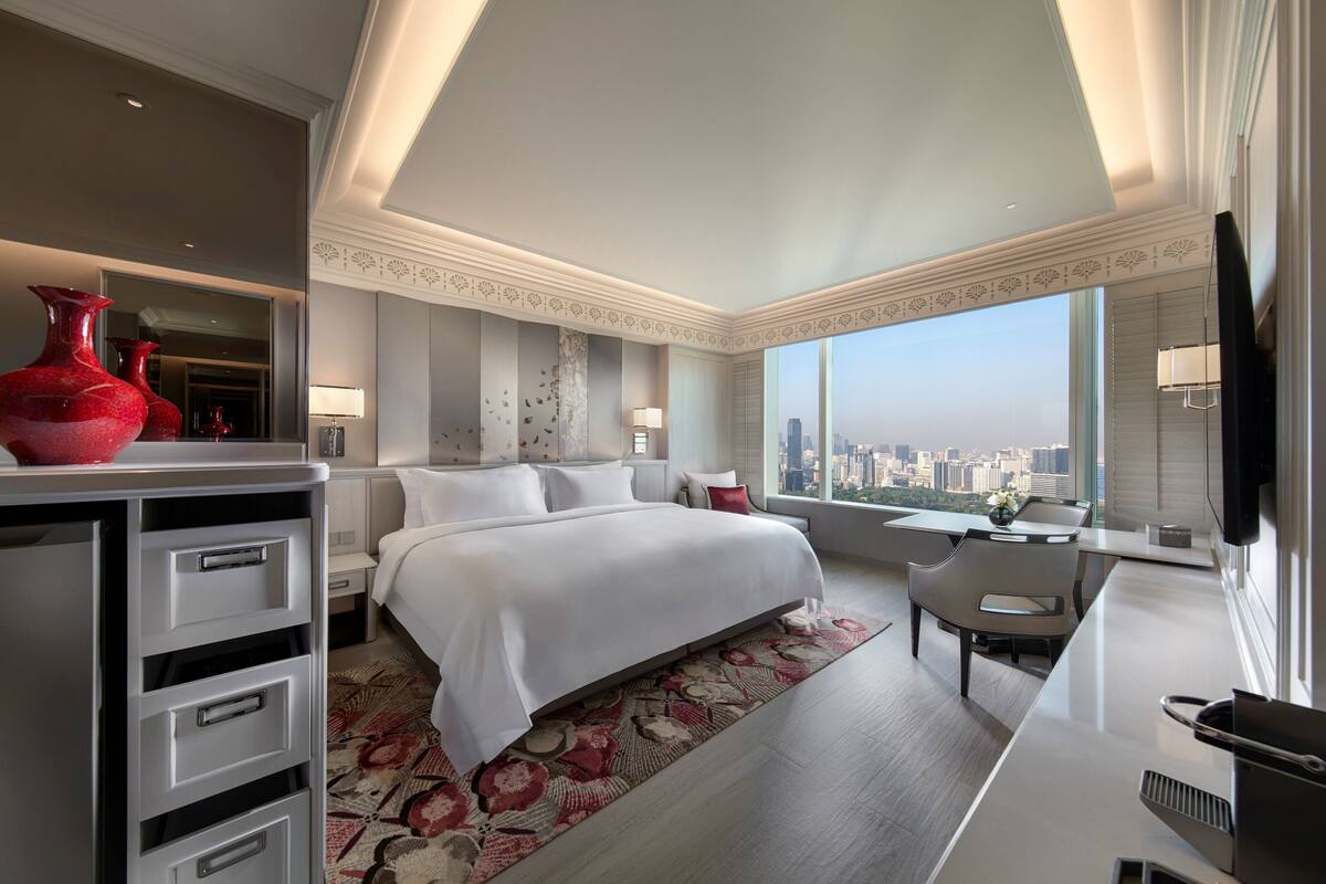 Une chambre d’hôtel moderne dotée d’un grand lit, d’un bureau et offrant une vue sur le panorama urbain.