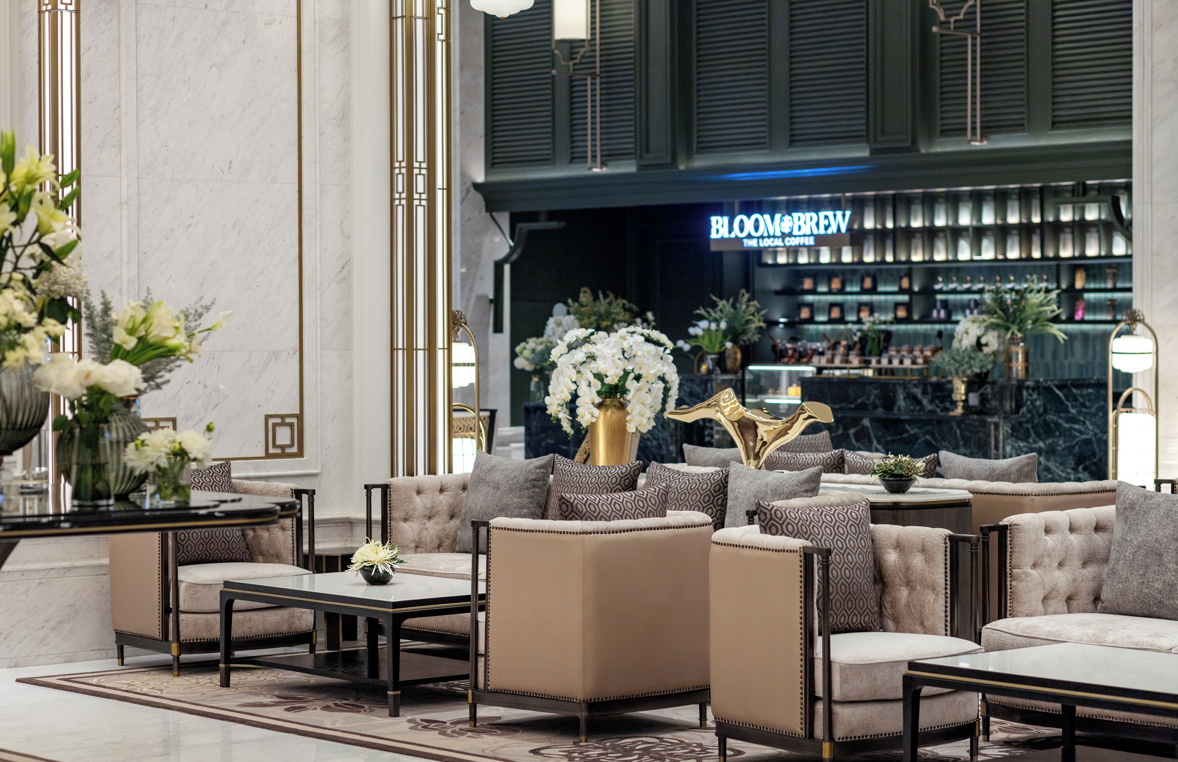 Un lobby lujoso con una zona de estar que incluye sofás y sillones, una barra de café al fondo y un piso de mármol.