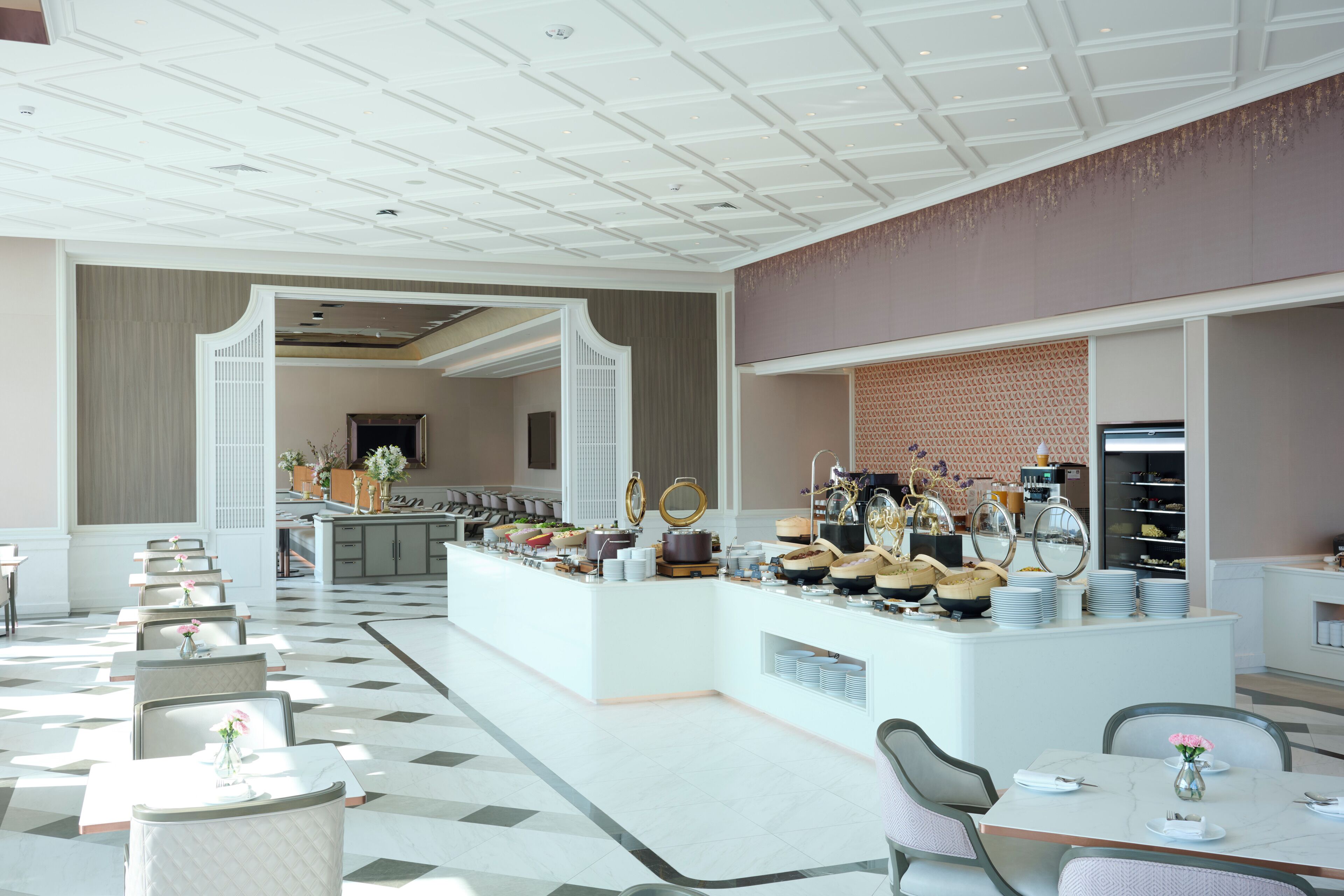 A spacious hotel lobby with a central buffet area, multiple seating arrangements, and a modern ceiling design.