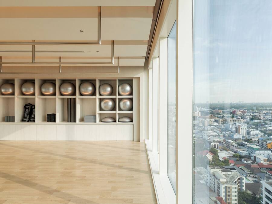 Amplia habitación con un ventanal que ofrece vistas a un paisaje urbano, suelo de madera y una estantería moderna con objetos esféricos.