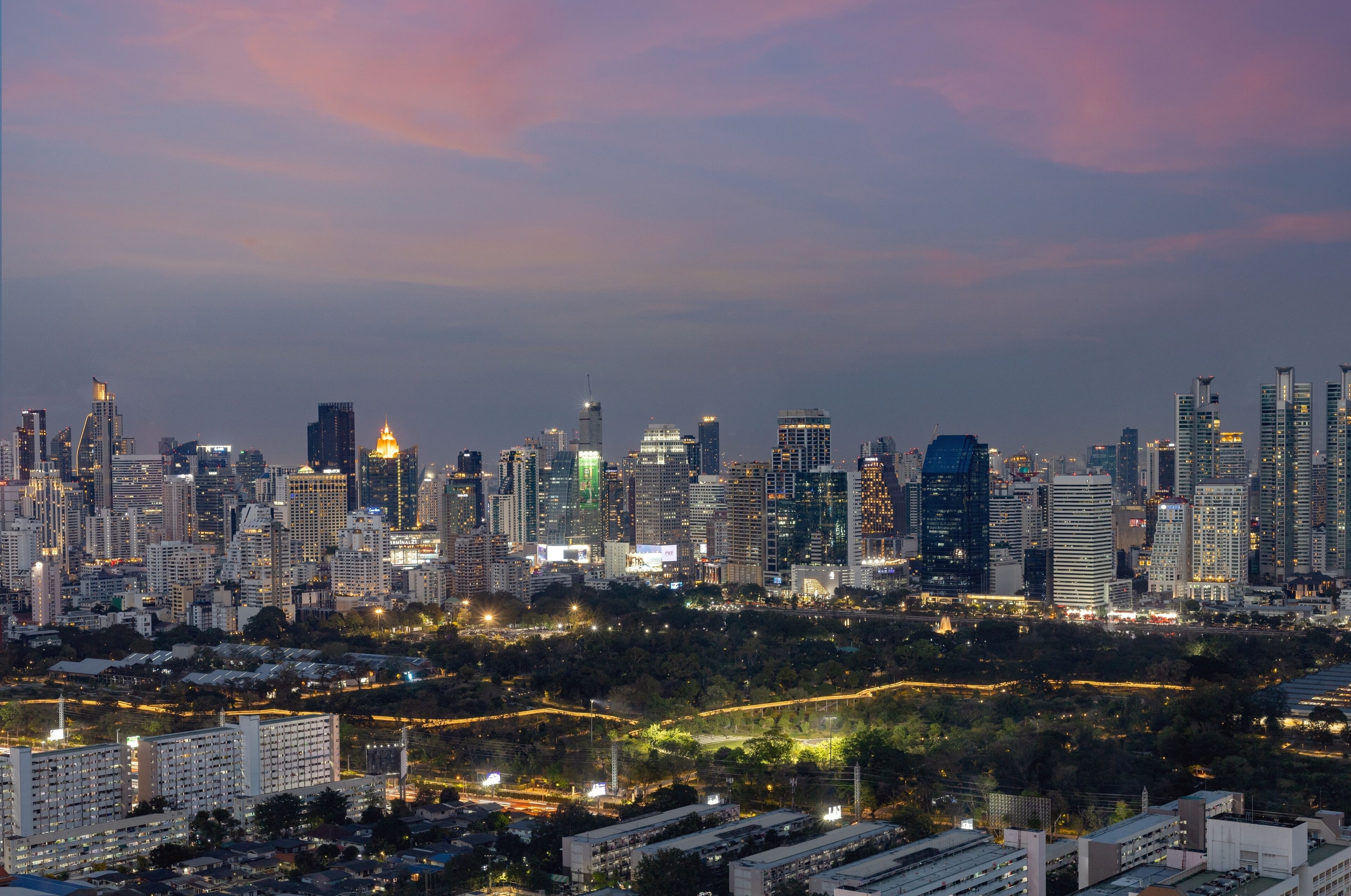 A city skyline at dusk with illuminated buildings and a dense urban area in the foreground.
