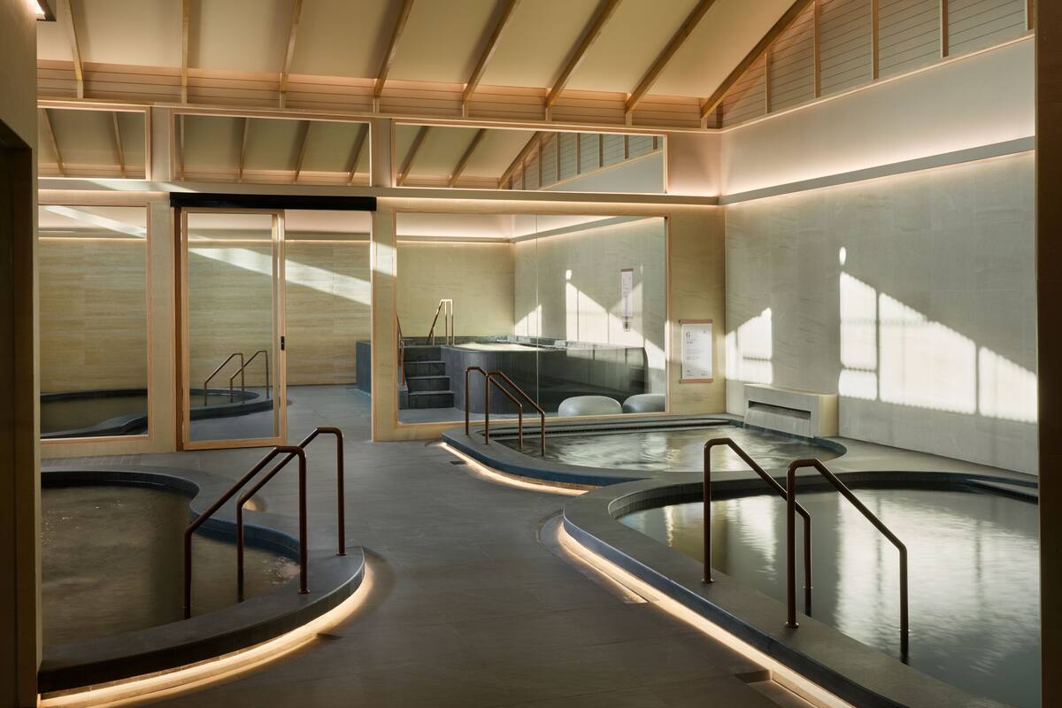 Un espace spa moderne doté d’un grand jacuzzi central, d’un escalier et d’un mur de verre offrant une vue sur l’extérieur.