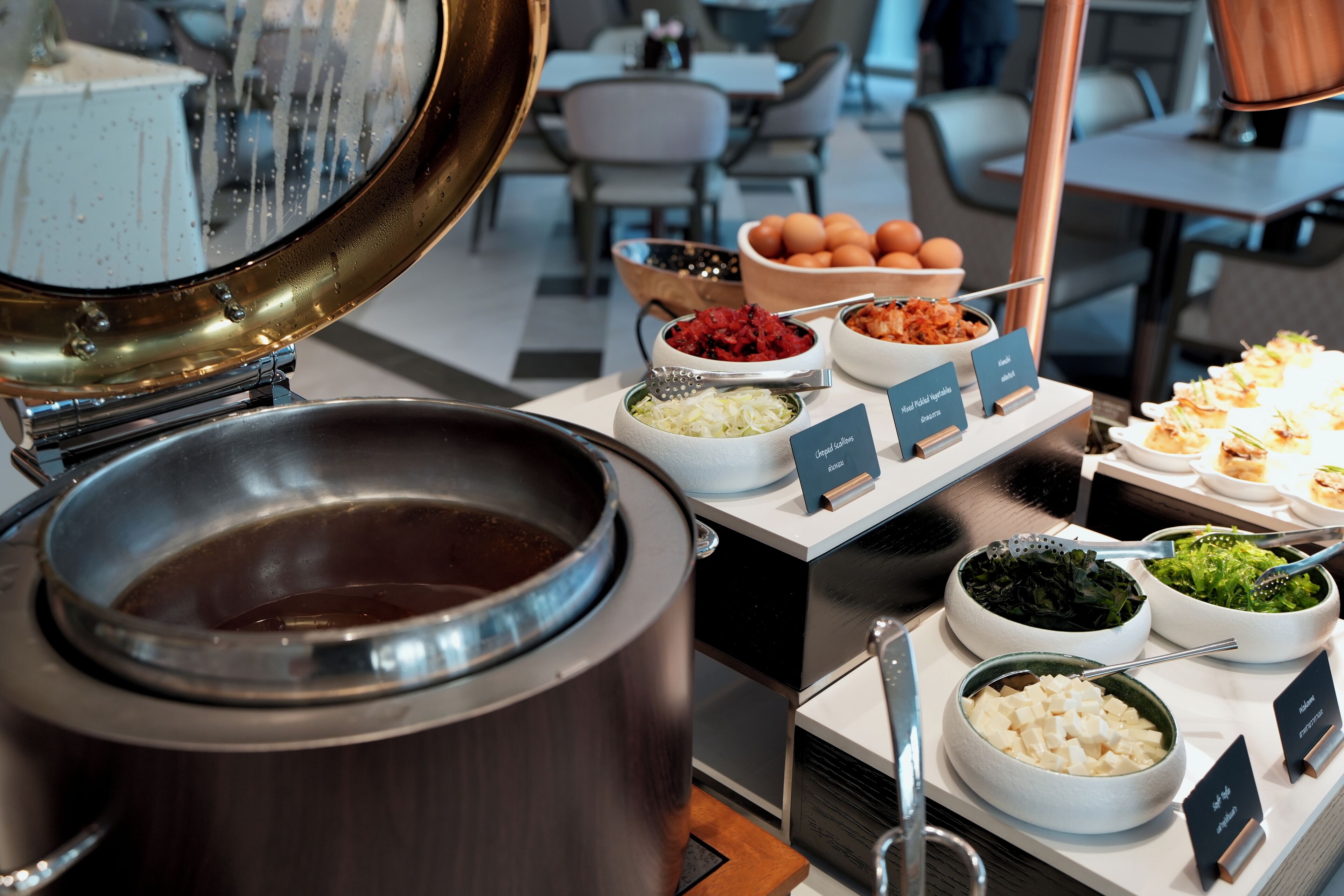 A buffet setup with various food items and a large pot of soup.
