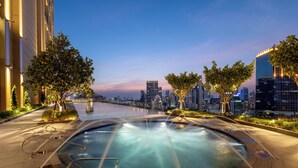 A cityscape with a pool area featuring a fountain, surrounded by trees and modern buildings.