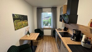 A compact kitchen with a dining area, a single window with curtains, a small table, and a dark green chair. - Apartment 'Ahlers' with Shared Terrace, Private Garden and Wi-Fi (Edewecht)
