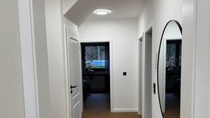 A hallway with white walls, wooden flooring, and a view of a blue building outside. - Apartment 'Ahlers' with Shared Terrace, Private Garden and Wi-Fi (Edewecht)