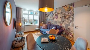 Una sala de estar moderna con un sofá, una mesa redonda con fruta, una lámpara colgante y un papel tapiz floral.