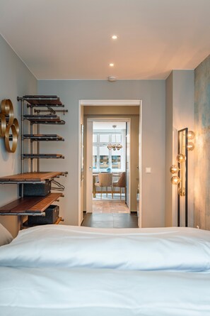 A modern hotel room with a bed, a wooden shelf unit, a mirror with lights, and a view into the dining area. - Apartment 'Fridolin Ca 45qm' with Wi-Fi (Lindau)