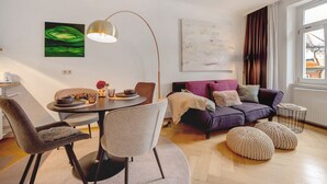 Un saló modern amb una taula rodona de menjador, dues cadires, un sofà i un finestra gran amb cortines.