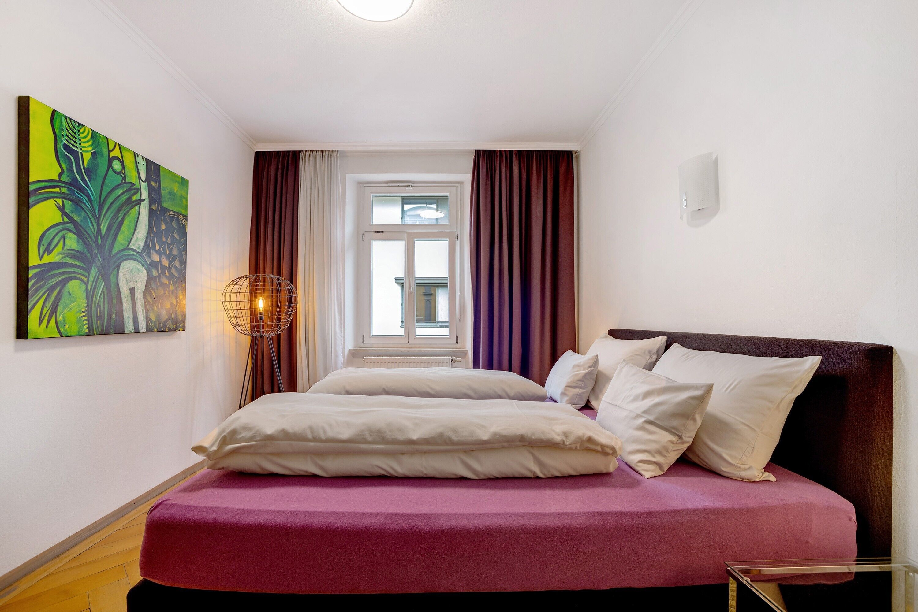 A bedroom with a bed, curtains, a window, and a wall-mounted light fixture.