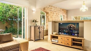 Un salon avec un mur en pierre, un téléviseur, un meuble en bois, un canapé et un tapis rouge.